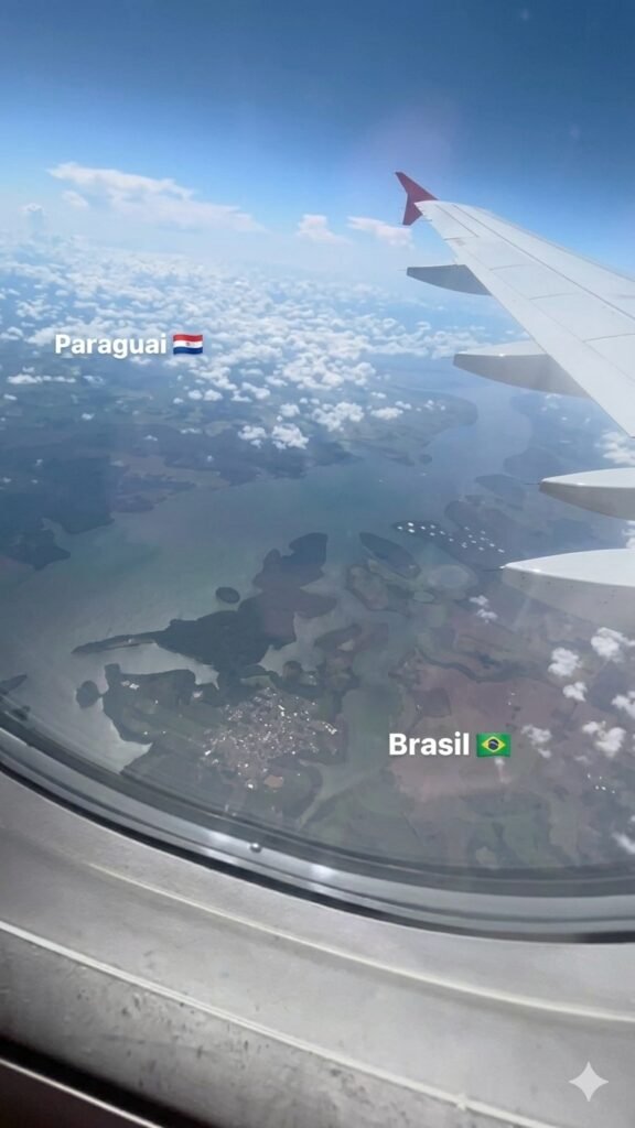 Visão aérea da fronteira Brasil-Paraguai pela janela do avião, destacando o rio que divide os países e as oportunidades de investimentos internacionais.